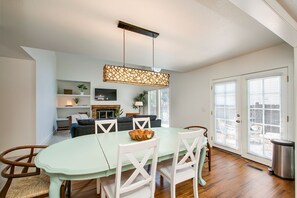 Un coin repas avec une table vert clair et des chaises blanches, un luminaire suspendu et une cheminée en arrière-plan.