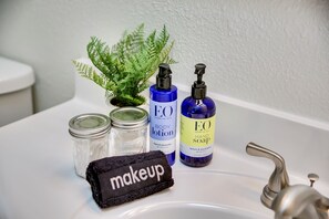 Un lavabo de salle de bain avec trois flacons d’huiles essentielles Eo, une petite plante en pot et une trousse de maquillage noire.