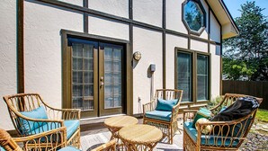 An outdoor patio with wicker furniture and a view of a building with large windows and shutters. - Elm Grove Elegance (Boise)