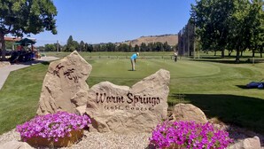 Un campo de golf con un cartel que dice 'Warm Springs Golf Course', rodeado de rocas y flores rosadas.