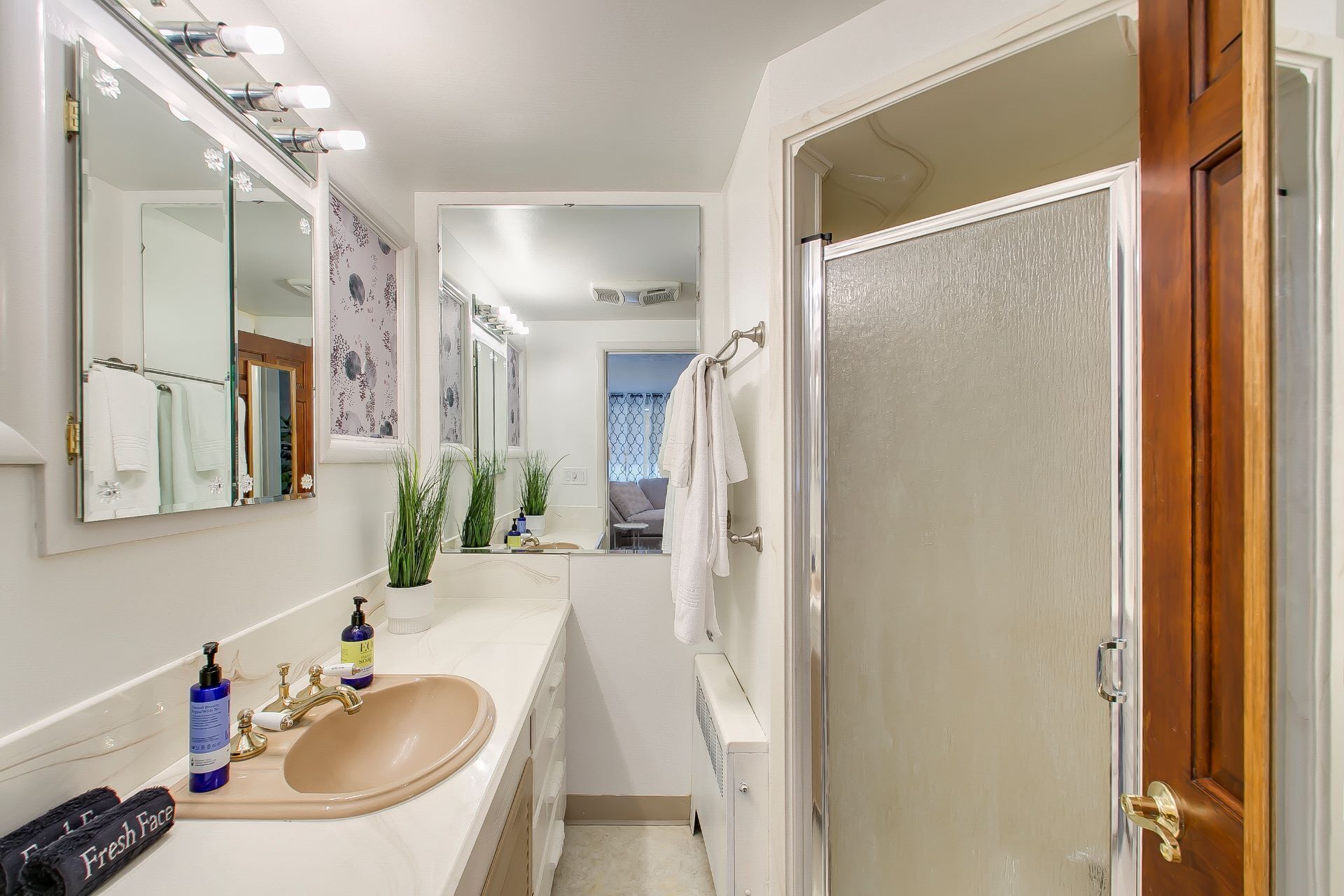 Une salle de bain avec un lavabo beige, un grand miroir et une porte de douche.
