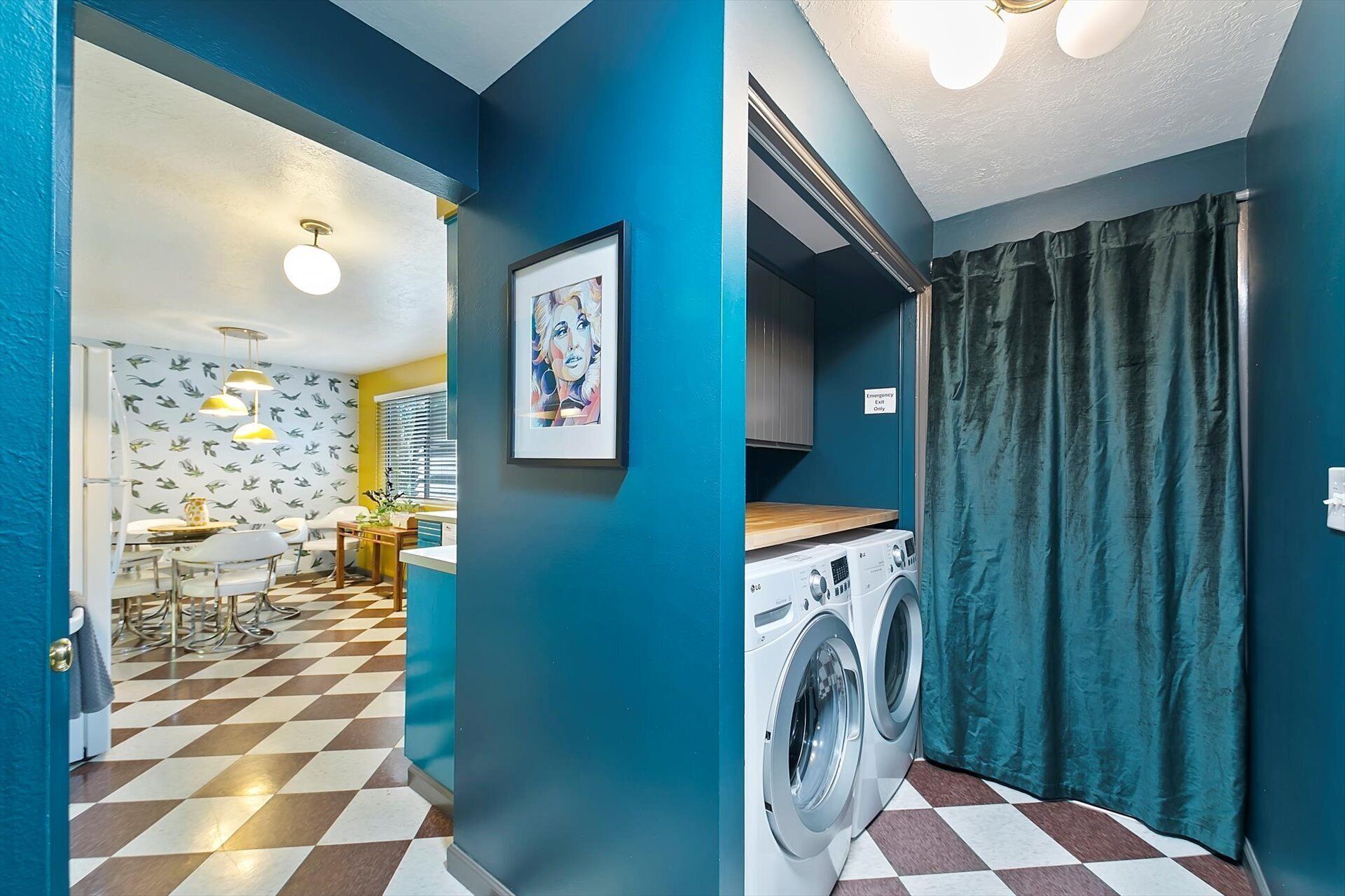 Un espacio habitable compacto con piso a cuadros, una lavadora, un comedor con mesa y sillas, y una pared de color verde azulado.
