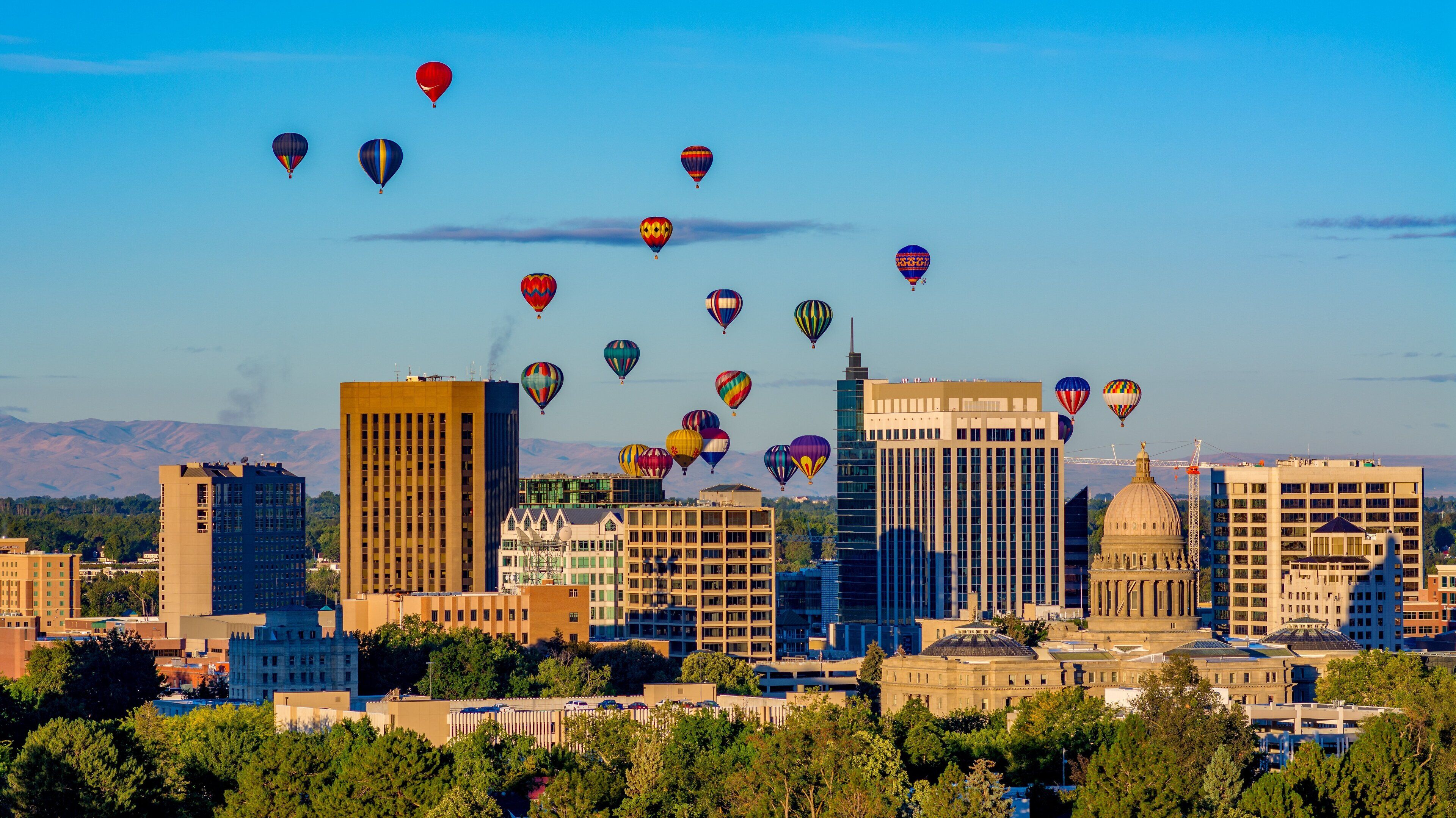 A cityscape with multiple buildings, including a prominent dome structure, and numerous hot air balloons in the sky.