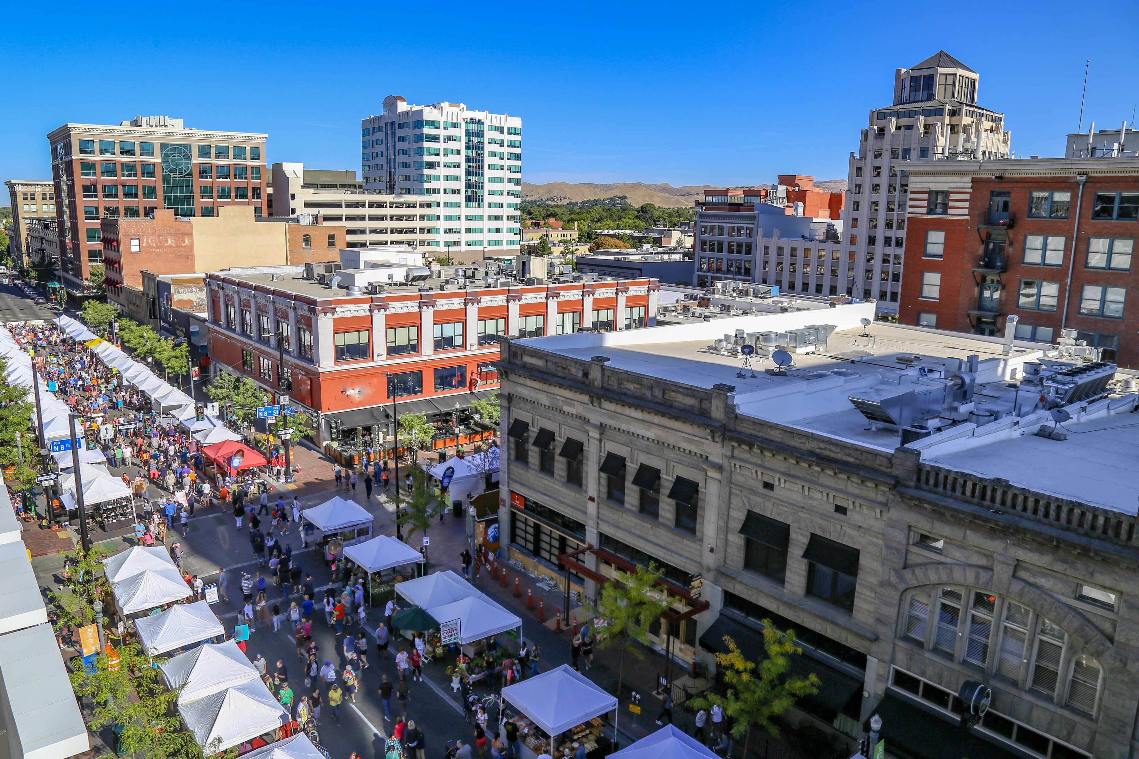 A bustling urban street with historic buildings, market stalls, and a clear blue sky.
