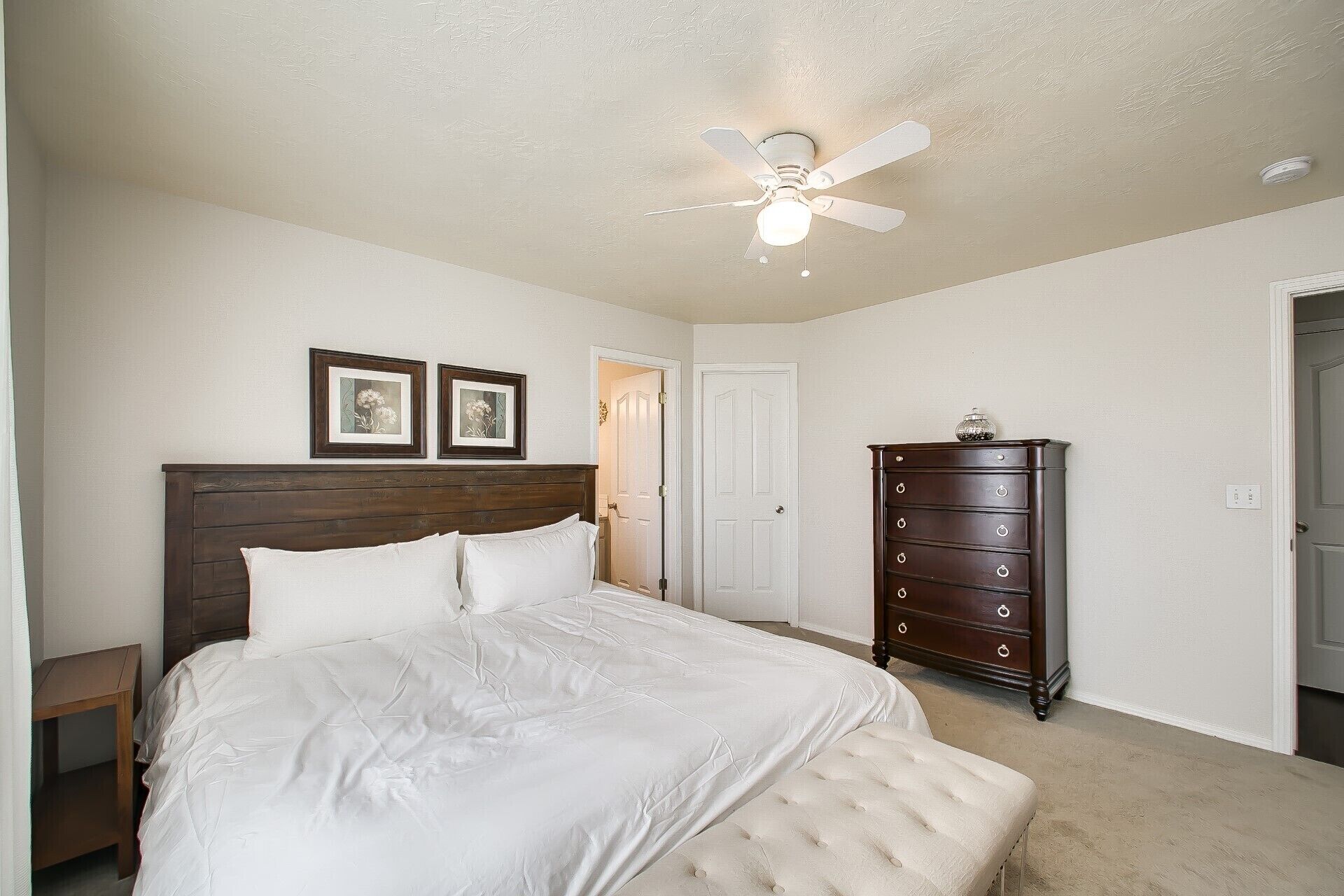 A bedroom with a bed, a dresser, a ceiling fan, and a door.