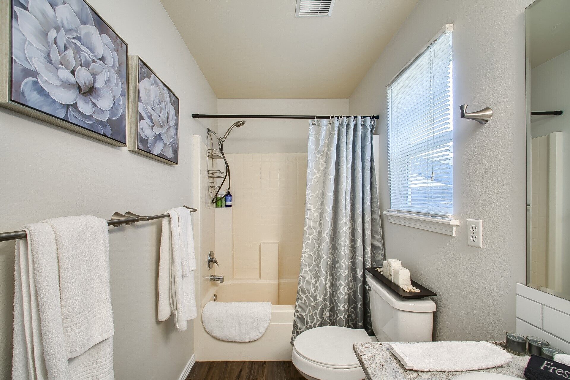 A bathroom with a shower, toilet, and sink. There are towels hanging on the wall and a window with blinds.