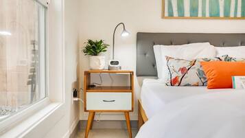 Un dormitorio con una cama, una mesita de noche con lámpara, un reloj y una planta.