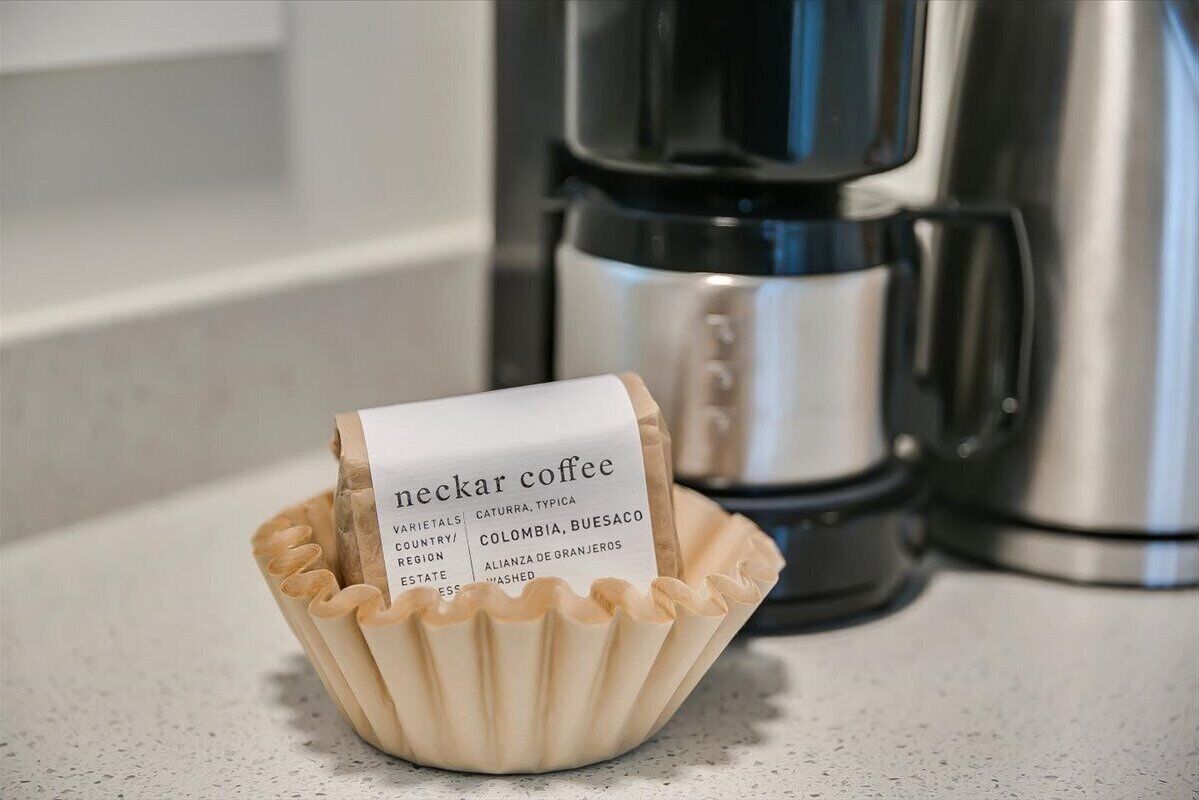 A paper label in a paper cup with text, placed on a countertop with a coffee maker in the background.
