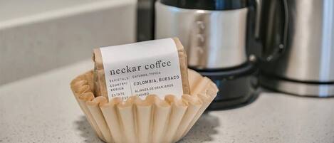 A paper label in a paper cup with text, placed on a countertop with a coffee maker in the background.