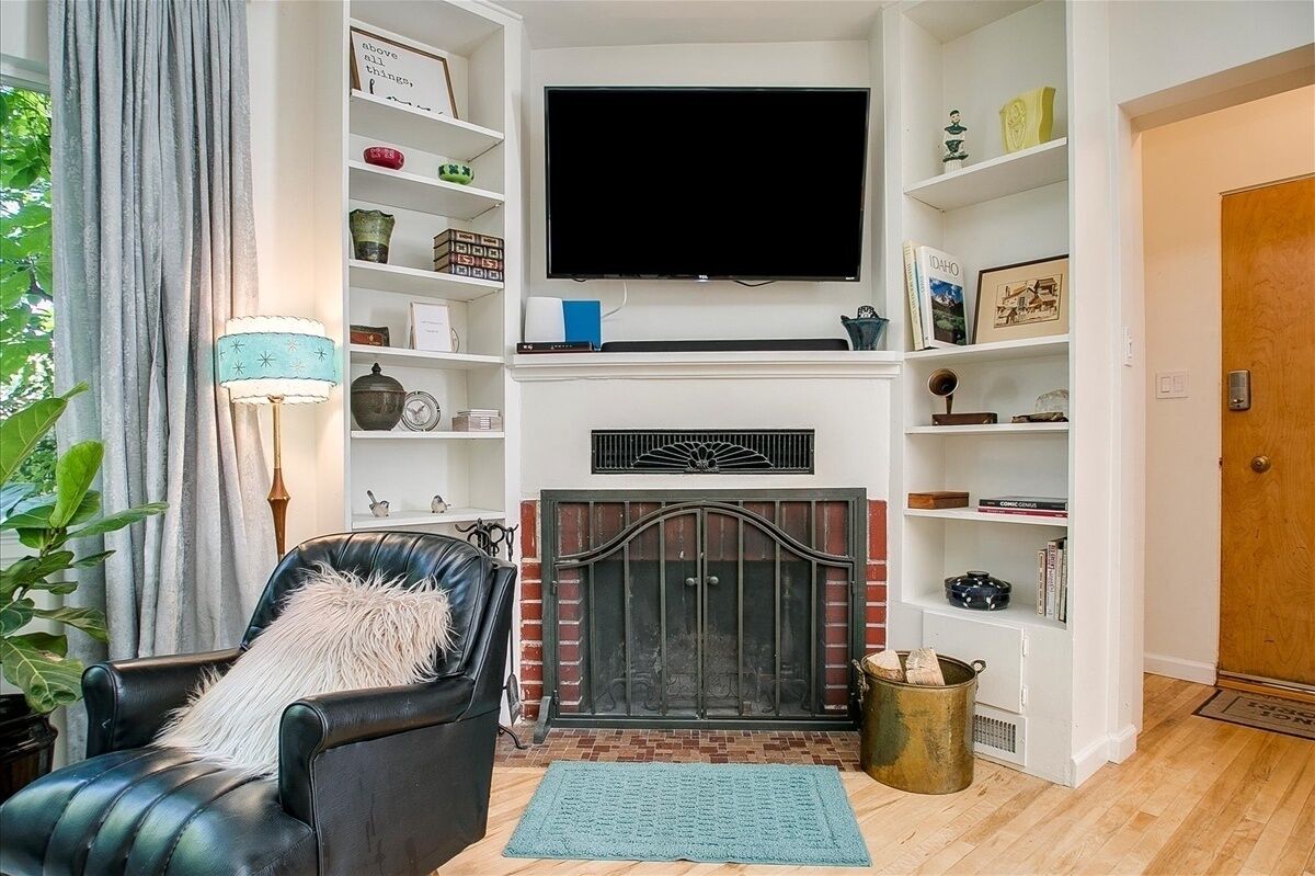 A living room with a fireplace, a television mounted above it, and a bookshelf filled with various items.