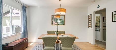 Un coin repas avec une table en bois, deux chaises, un luminaire suspendu et un tapis à motifs.