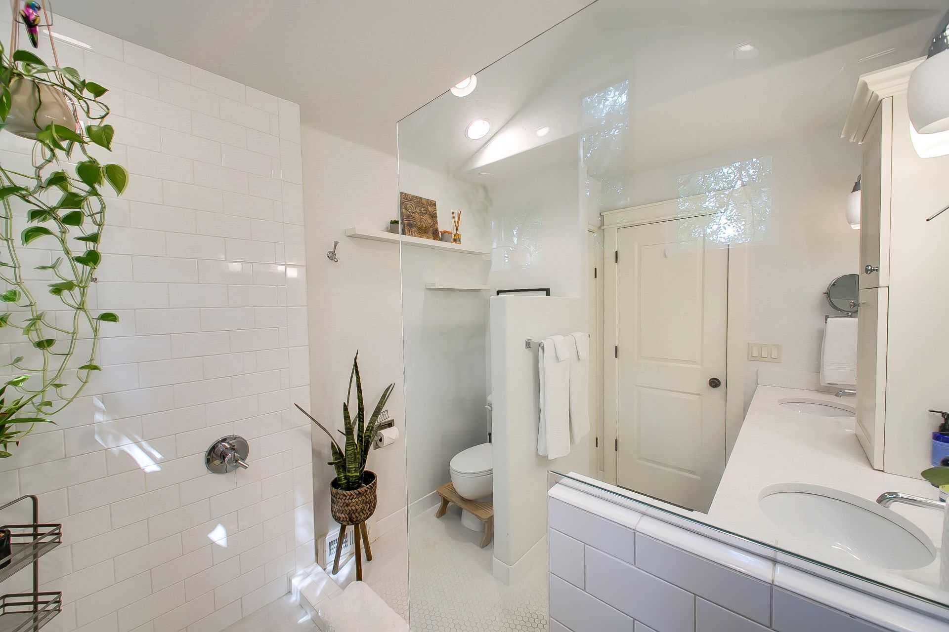 Un baño moderno con azulejos blancos, cabina de ducha de cristal, inodoro y lavabo con espejo.
