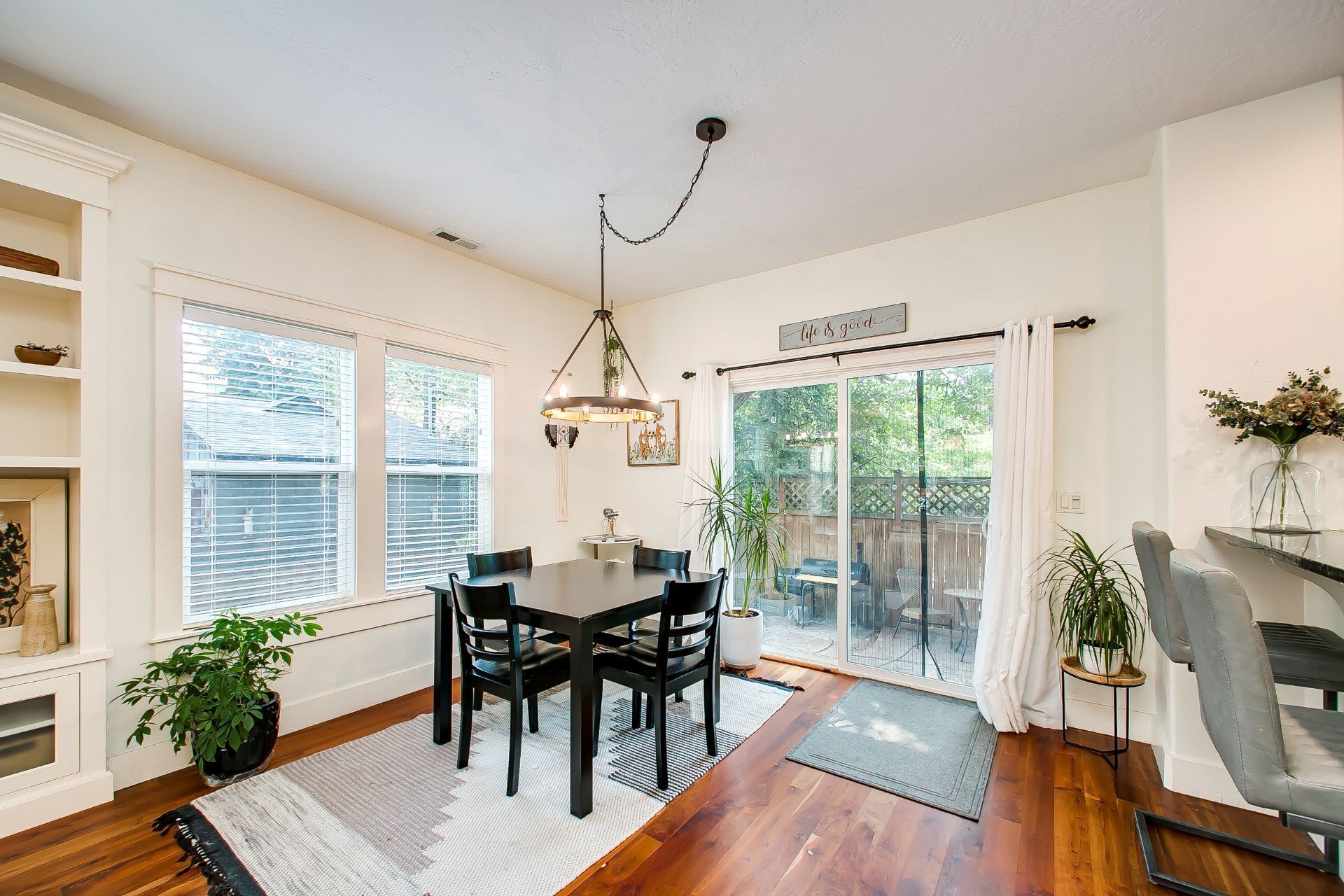 A dining area with a table and chairs, a hanging light fixture, and a view through a glass door to an outdoor patio.
