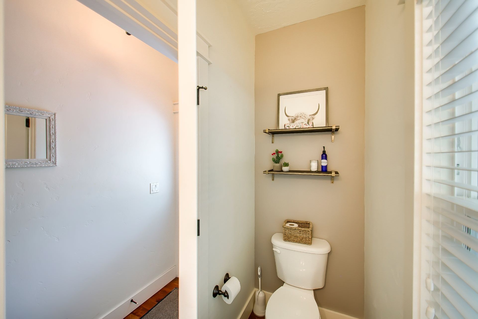 A bathroom with a toilet, a mirror, and a shelf with a framed picture and toiletries.