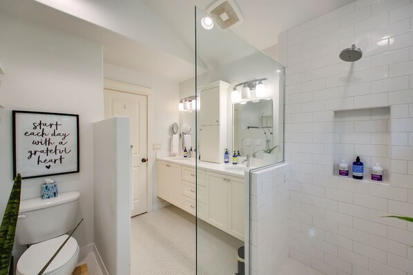 Un baño moderno con cabina de ducha de vidrio, azulejos blancos y una cita inspiradora enmarcada en la pared.