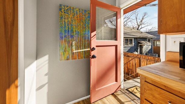 A hallway with a wooden door, a colorful painting, and a view of a backyard. - Red Ivy #5 (Boise)