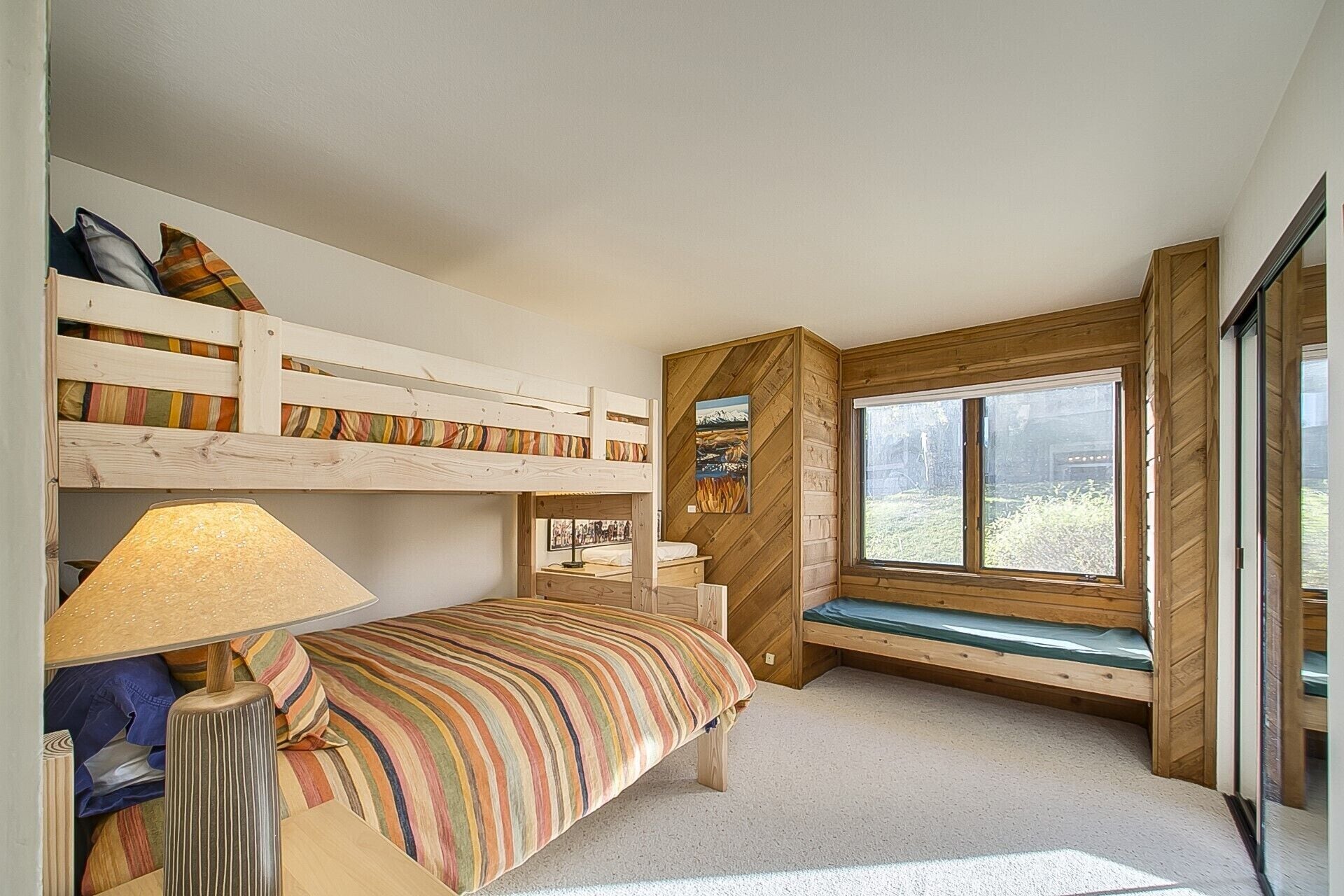 A bedroom with bunk beds, a bedside lamp, a window with a view, and a wooden wall panel.