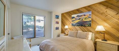 A bedroom with a large bed, wooden panel wall, and a window with a view of the outside.