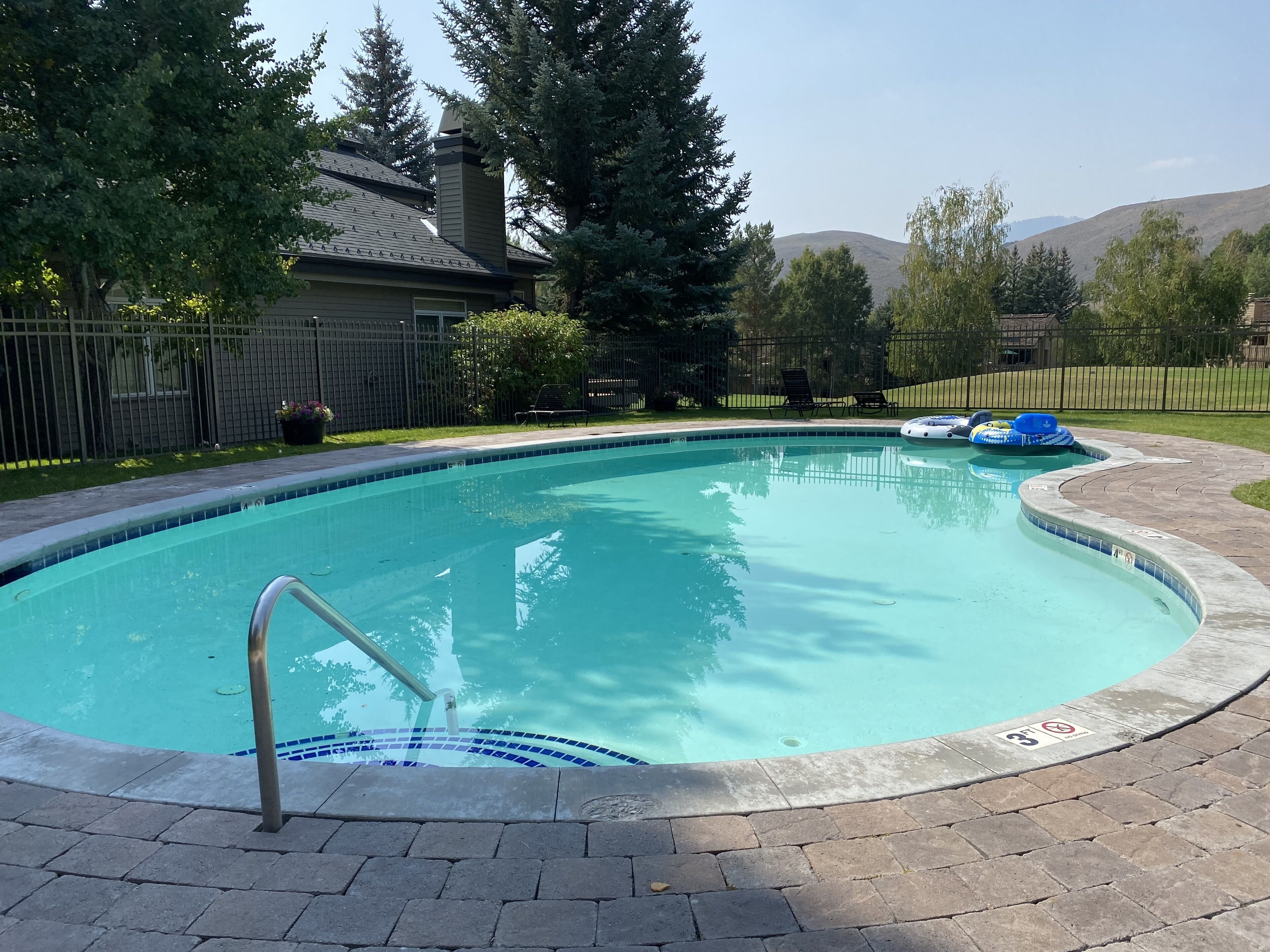Piscina com borda revestida de azulejos, escada de metal e área pavimentada ao redor.