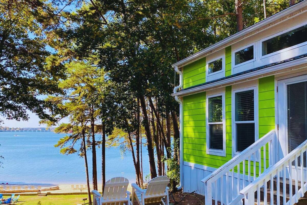 A bright green house with white trim, a porch, and a view of the water.
