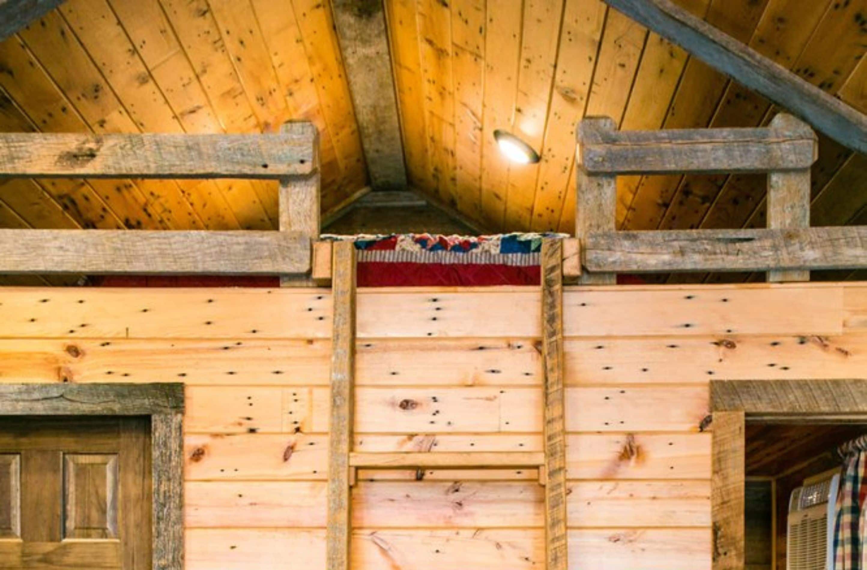 Ein Holzblockbau mit schrägem Dach, einer zentralen Holztreppe und einer Tür links.