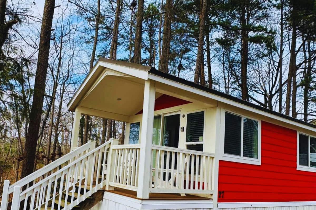 A cabin with a white porch and red siding, surrounded by tall trees.