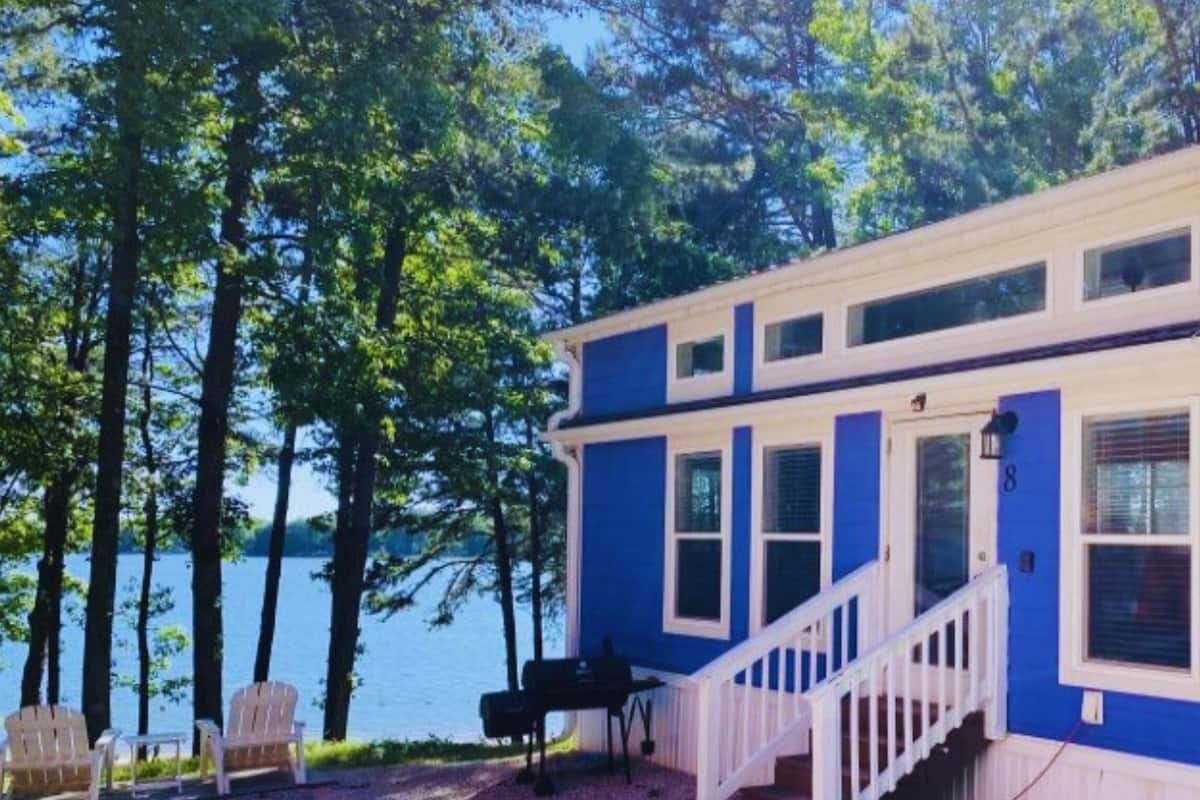 A lakeside cabin with a covered deck, a staircase, and a view of the water.