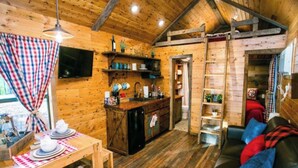A cozy cabin interior with a wooden dining table set, a black refrigerator, a wooden sofa with cushions, and a television mounted on the wall. - Long Cove Resort near Charlotte Airport (Charlotte)