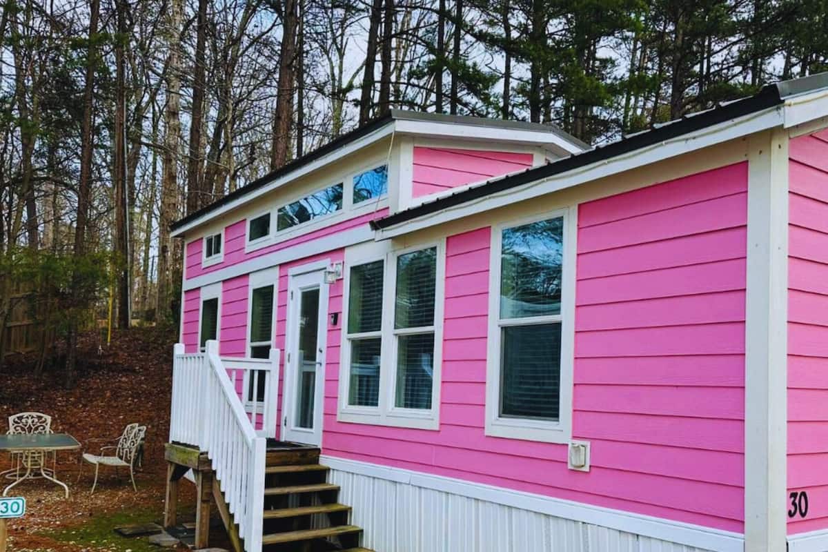 A pink house with a white porch and steps, surrounded by trees.