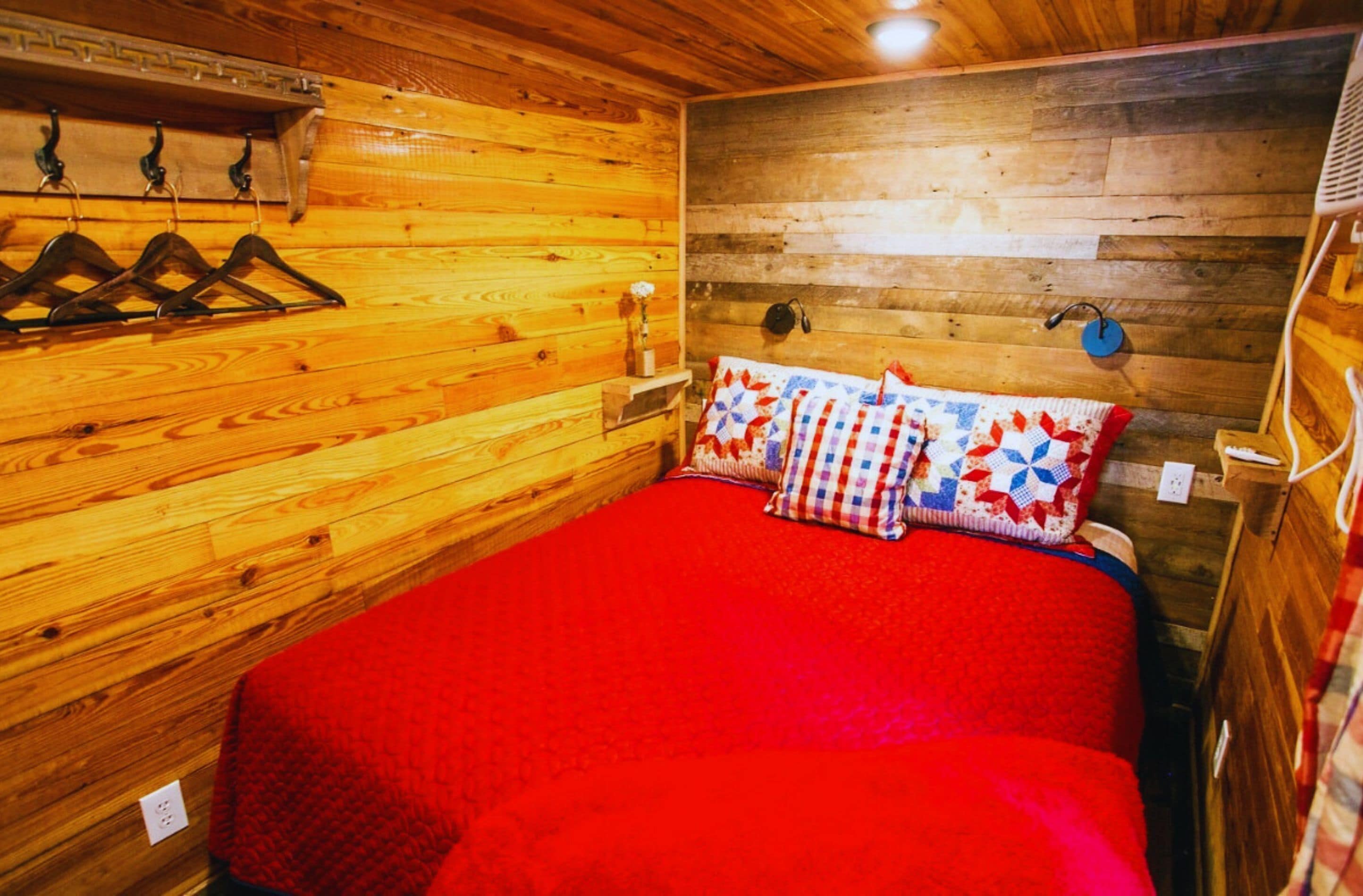 A wooden cabin room with a bed, wooden walls, and a red blanket.