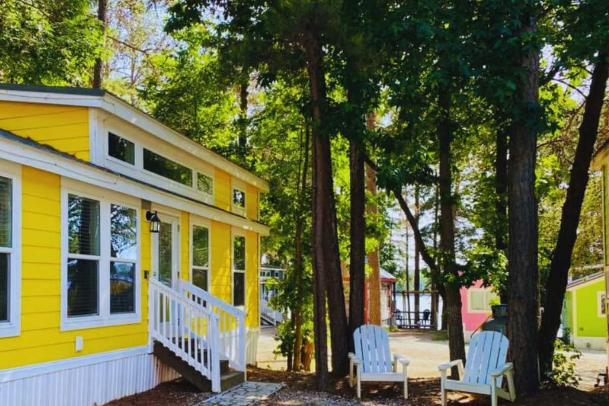 A yellow building with a white porch and steps, surrounded by trees.