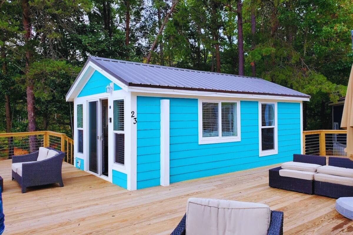 A small, two-story house with a blue exterior and white trim. It features a deck with outdoor furniture and a number '2' visible on the side.