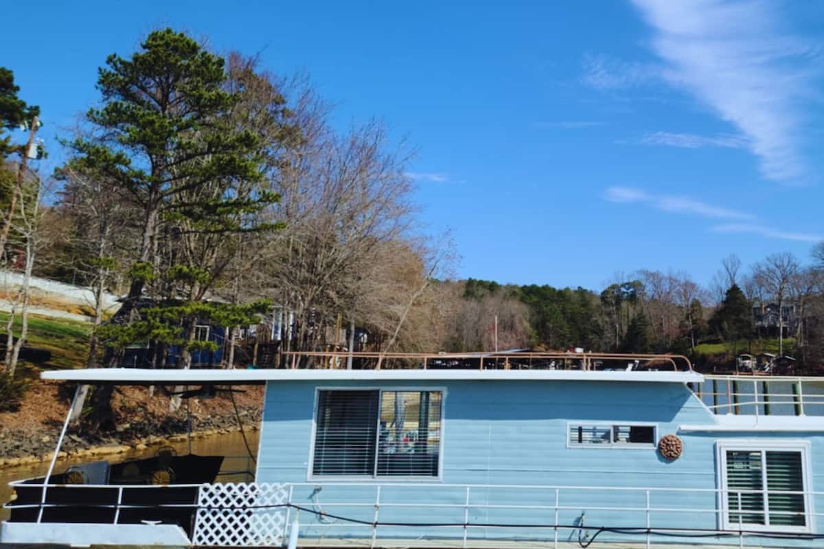 A blue houseboat with a white deck, windows, and a small porch area.