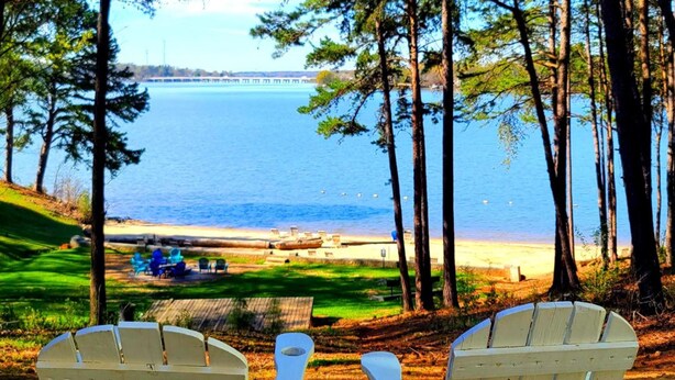 A view of a beach with chairs and a table, overlooking a body of water and a distant bridge. - Long Cove Resort near Charlotte Airport (Charlotte)