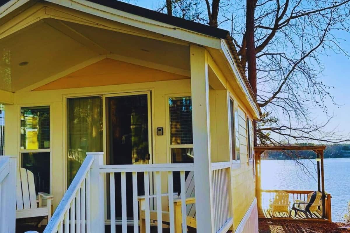 A small, single-story cabin with a porch and a view of a lake.