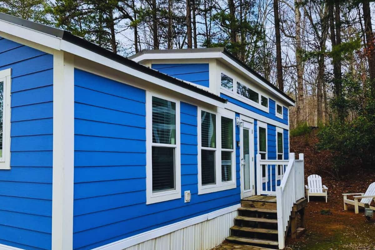 A blue cabin with white trim, a front porch, and a small deck with chairs.