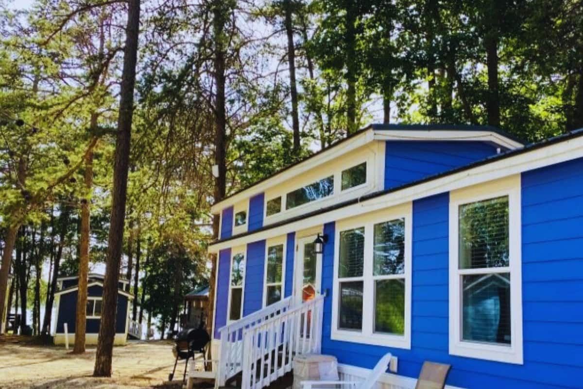 A blue building with a white porch and windows, surrounded by trees.