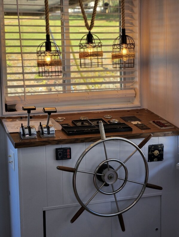 Una encimera de cocina con un timón de barco, una estufa y una ventana con persianas.