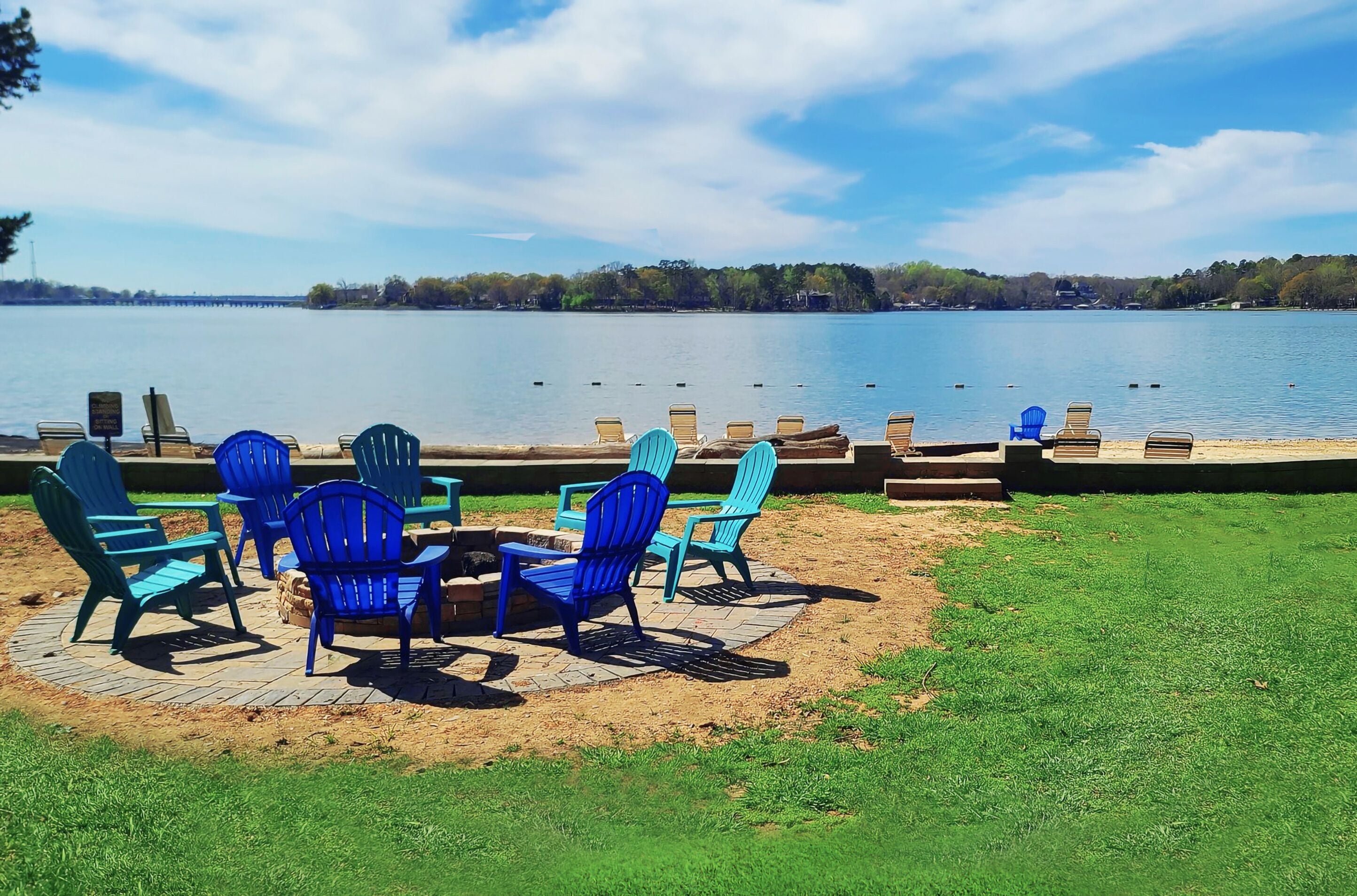 Outdoor seating with chairs and a table by a lake, with a dock and trees in the background.