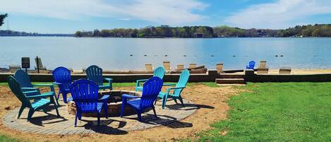 Outdoor seating with chairs and a table by a lake, with a dock and trees in the background.