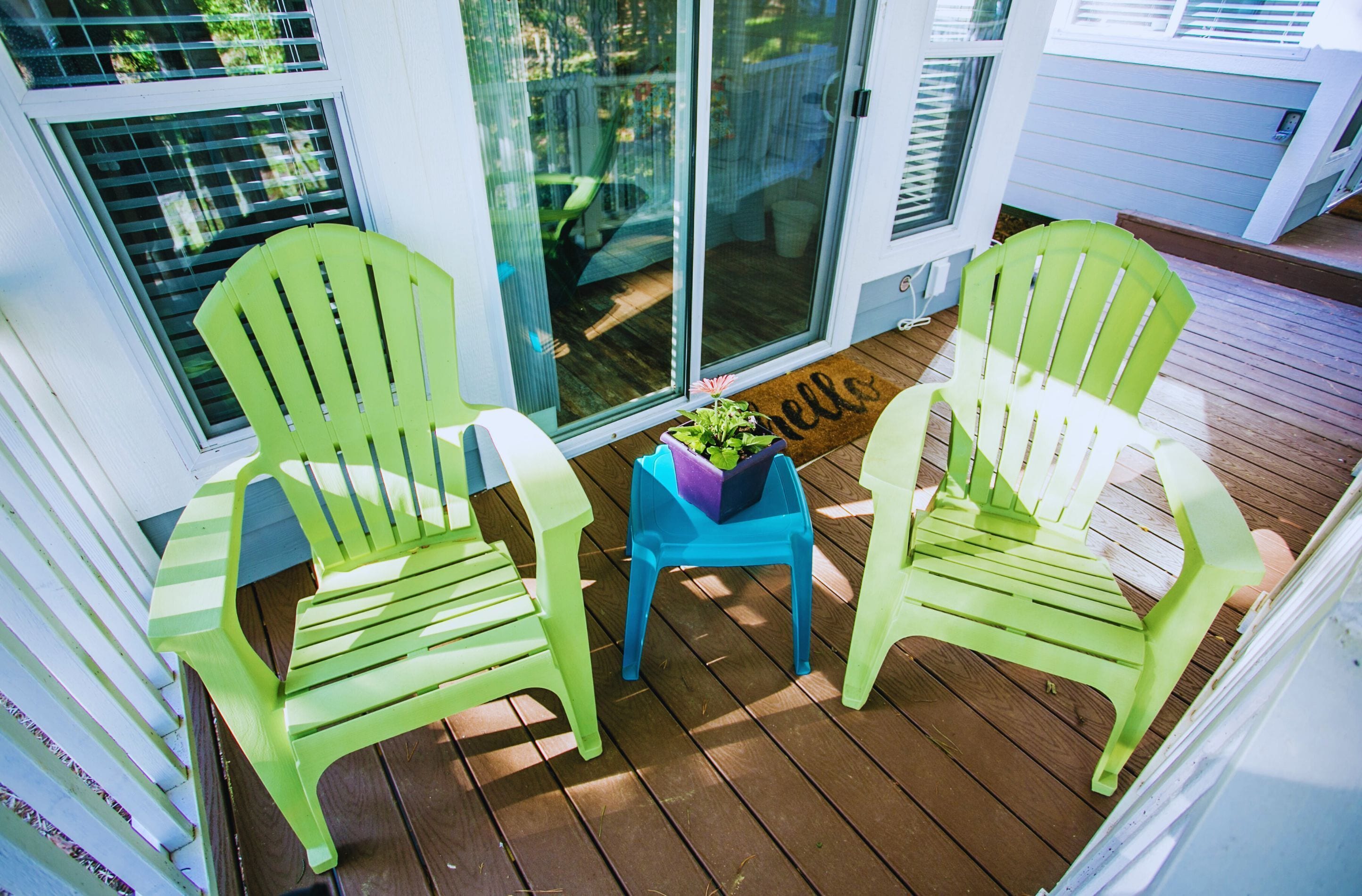 A wooden deck with two green chairs and a small table with a plant.
