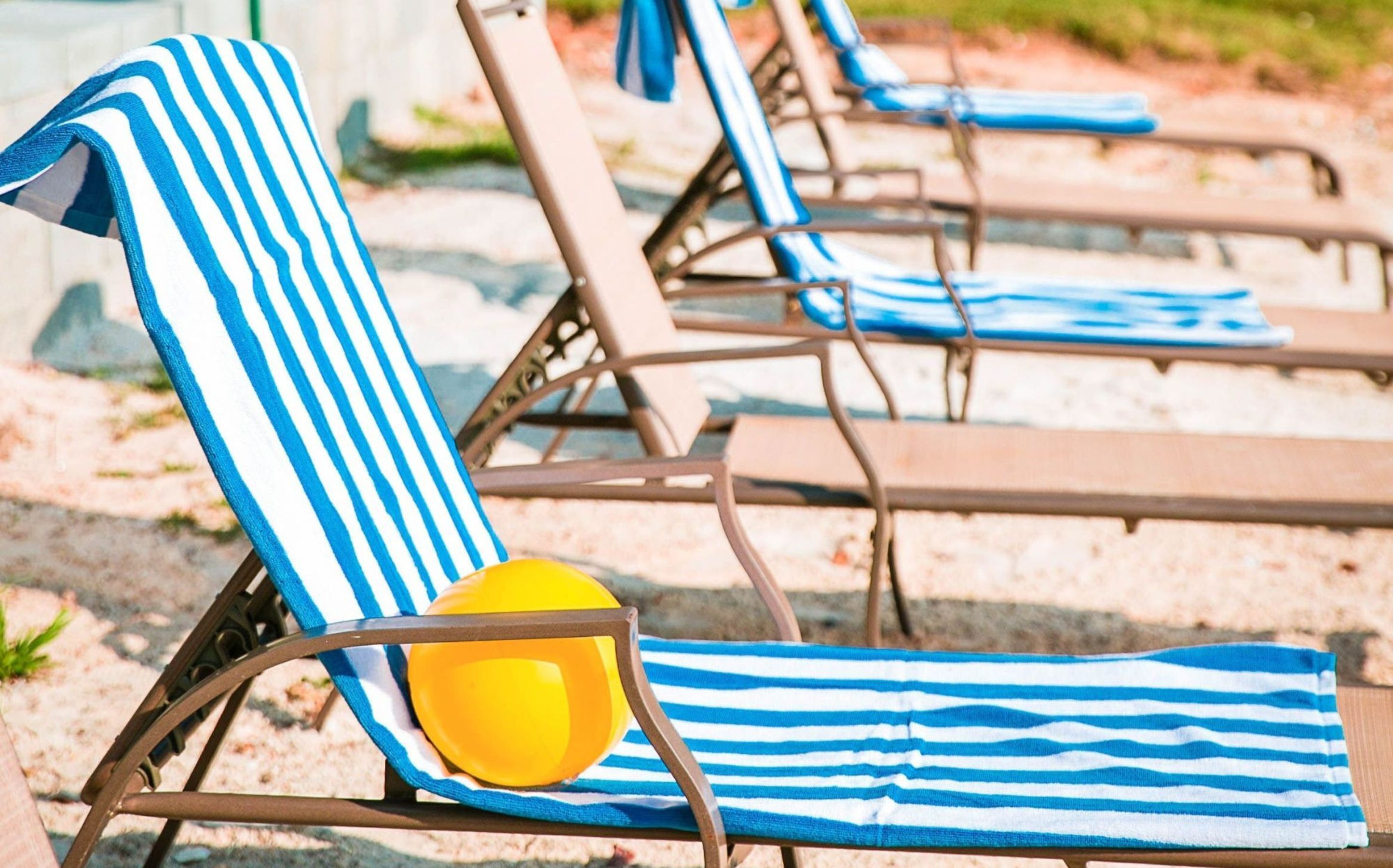 A row of beach chairs with blue and white striped towels and a yellow beach ball.