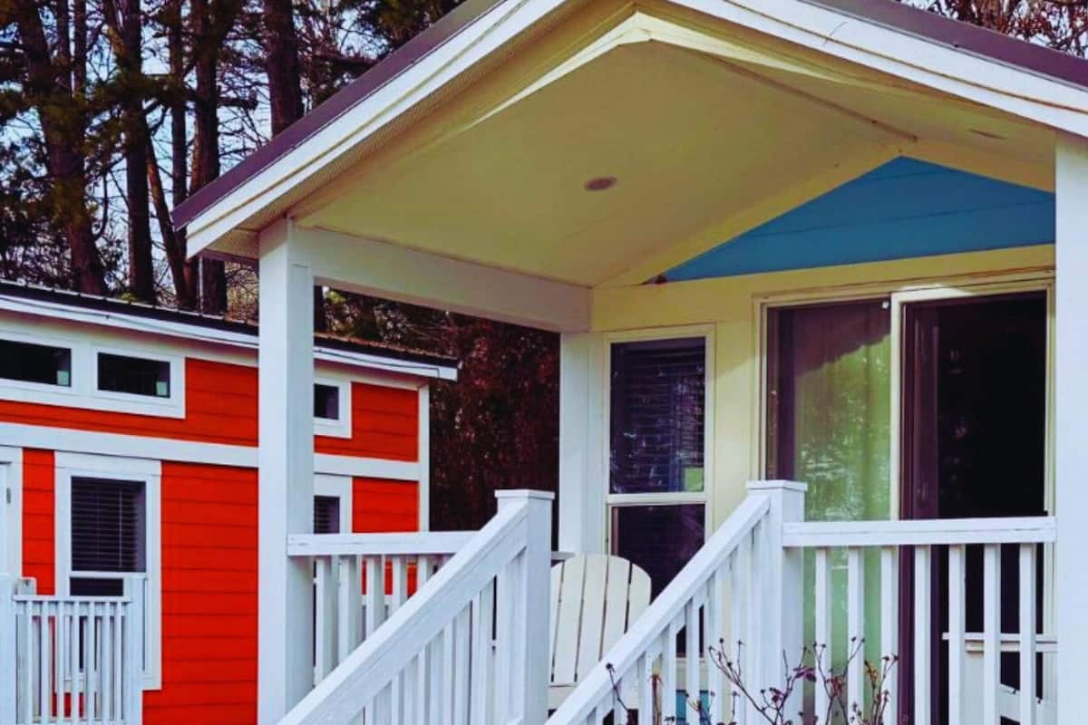 A small, single-story house with a porch, white railings, and a blue and yellow exterior.