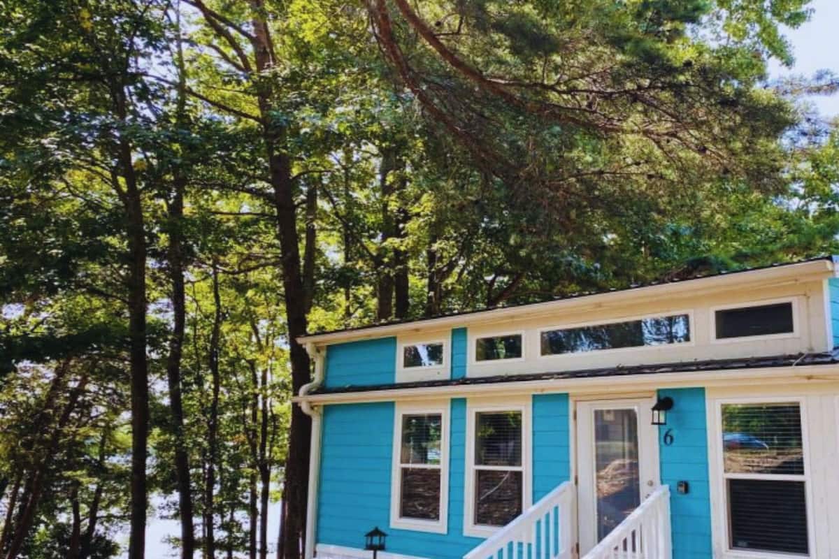 A two-story house with a blue exterior and white trim, surrounded by tall trees.