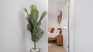 A hallway with a potted plant, a bed with a nightstand, and a wall-mounted artwork. - Basalt Dwelling I by Homie (São Vicente)
