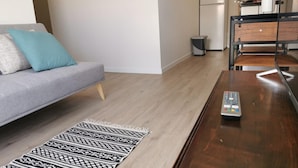 A modern living room with a grey sofa, a patterned rug, a wooden coffee table, and a kitchen area in the background. - Basalt Dwelling I by Homie (São Vicente)