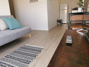 Ein modernes Wohnzimmer mit einem grauen Sofa, einem gemusterten Teppich, einem Holztisch und einer Küchenzeile im Hintergrund.