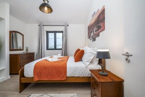 Ein modernes Schlafzimmer mit einem hölzernen Bett, einem Nachttisch mit Lampe, einem Fenster mit Vorhängen und einem Gemälde an der Wand.