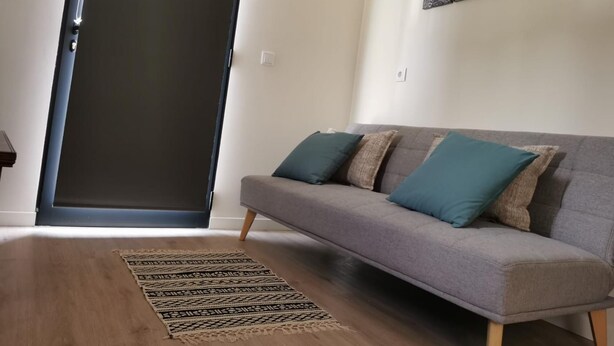 A living room with a grey sofa, patterned rug, and a door. - Basalt Dwelling I by Homie (São Vicente)