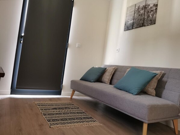Ein Wohnzimmer mit grauem Sofa, Teppich mit Muster und einer Tür.